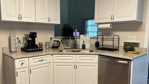 A kitchen with white cabinets, a coffee maker, a kettle, and a fruit bowl. - Beautiful Family Home  (Tallahassee)