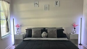 A bedroom with a large bed, two bedside tables, a window with curtains, and wall-mounted artwork. - Beautiful Family Home  (Tallahassee)