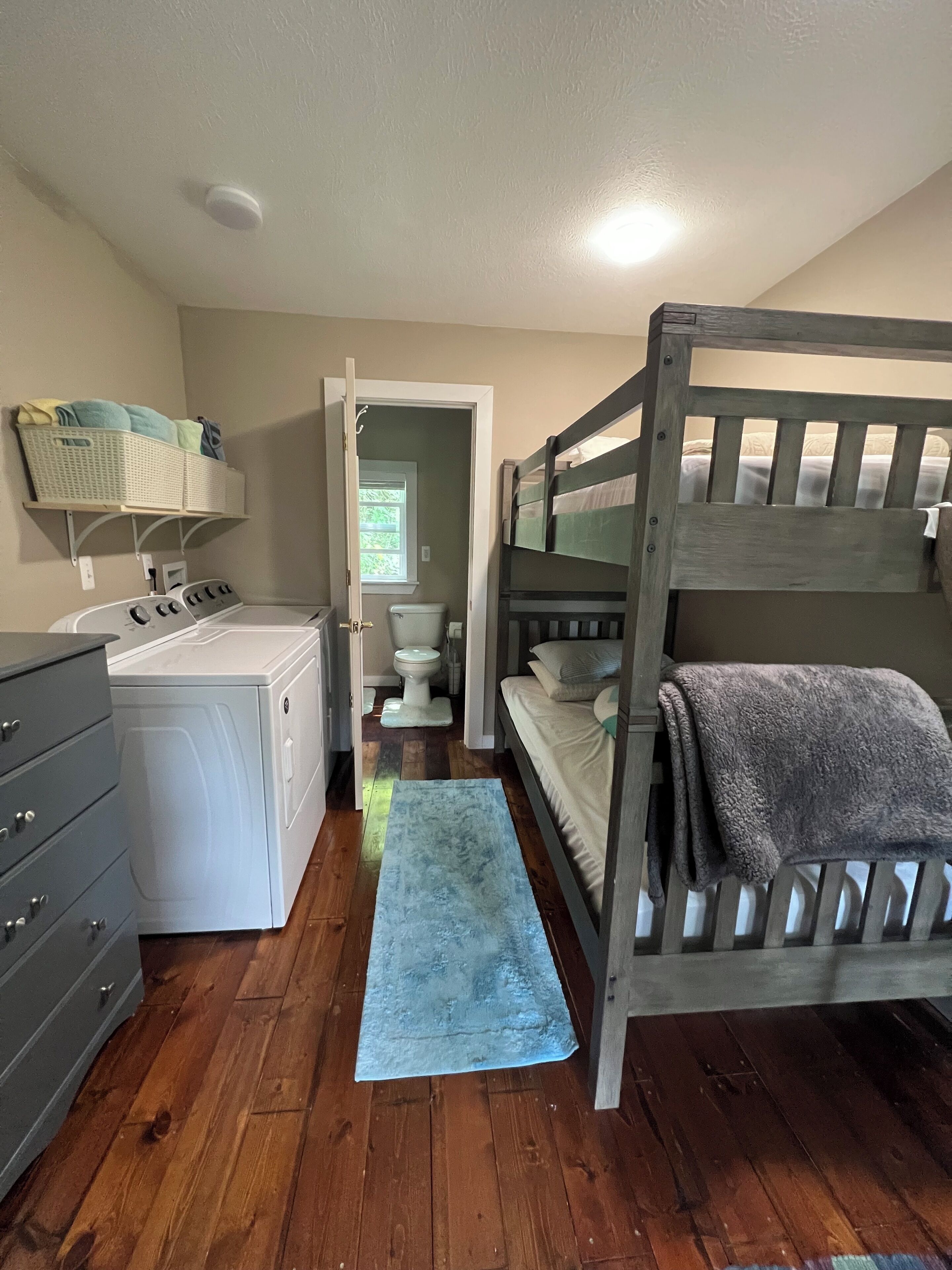 A compact bedroom with a bunk bed, a washing machine, a dryer, and a small bathroom.