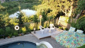 A pool with a curved edge, surrounded by a patio area with white chairs and a table. There is a bed with a floral bedspread and a view of a lake and greenery. - A family-friendly getaway, with outdoor pool and beautiful view!
(Newmarket)