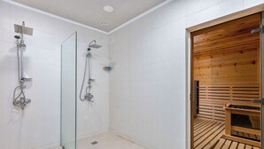 Ein modernes Badezimmer mit einer Duschkabine aus Glas, einer Holztür zur Sauna und einem gefliesten Boden.