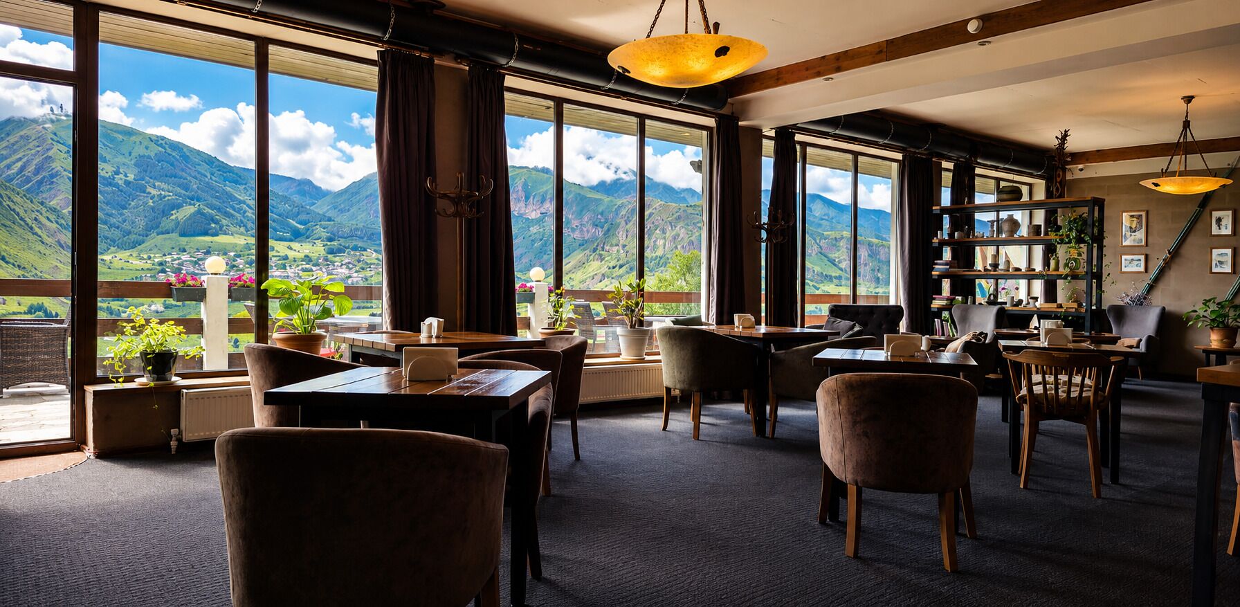 A hotel room with large windows, a dining area, and a view of mountains.