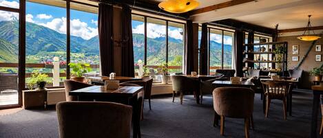 A hotel room with large windows, a dining area, and a view of mountains.