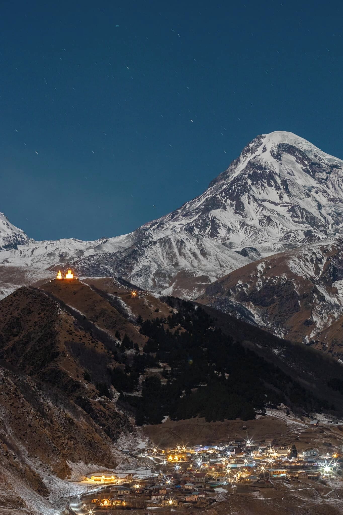 Ein schneebedeckter Berg bei Nacht mit einer Stadt darunter.
