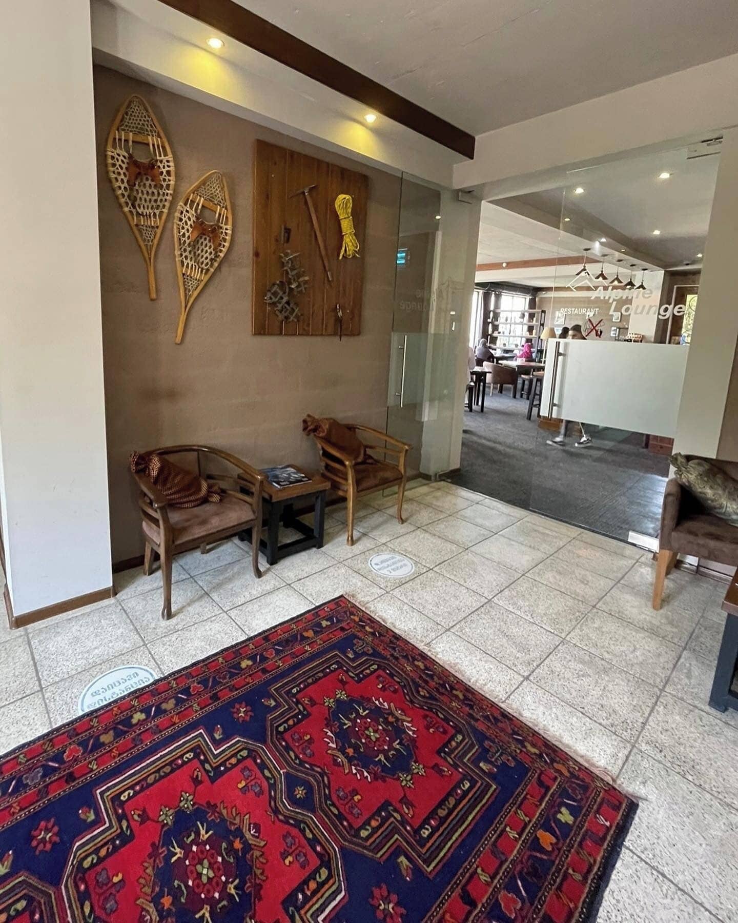 Un vestíbulo con alfombra estampada, sillas de madera, una mesita y cuadros en la pared.