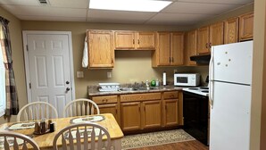 A compact kitchen with wooden cabinets, a white refrigerator, a microwave, and a dining area with a table and chairs. - Gound level and private home with river front access. (Ronceverte)