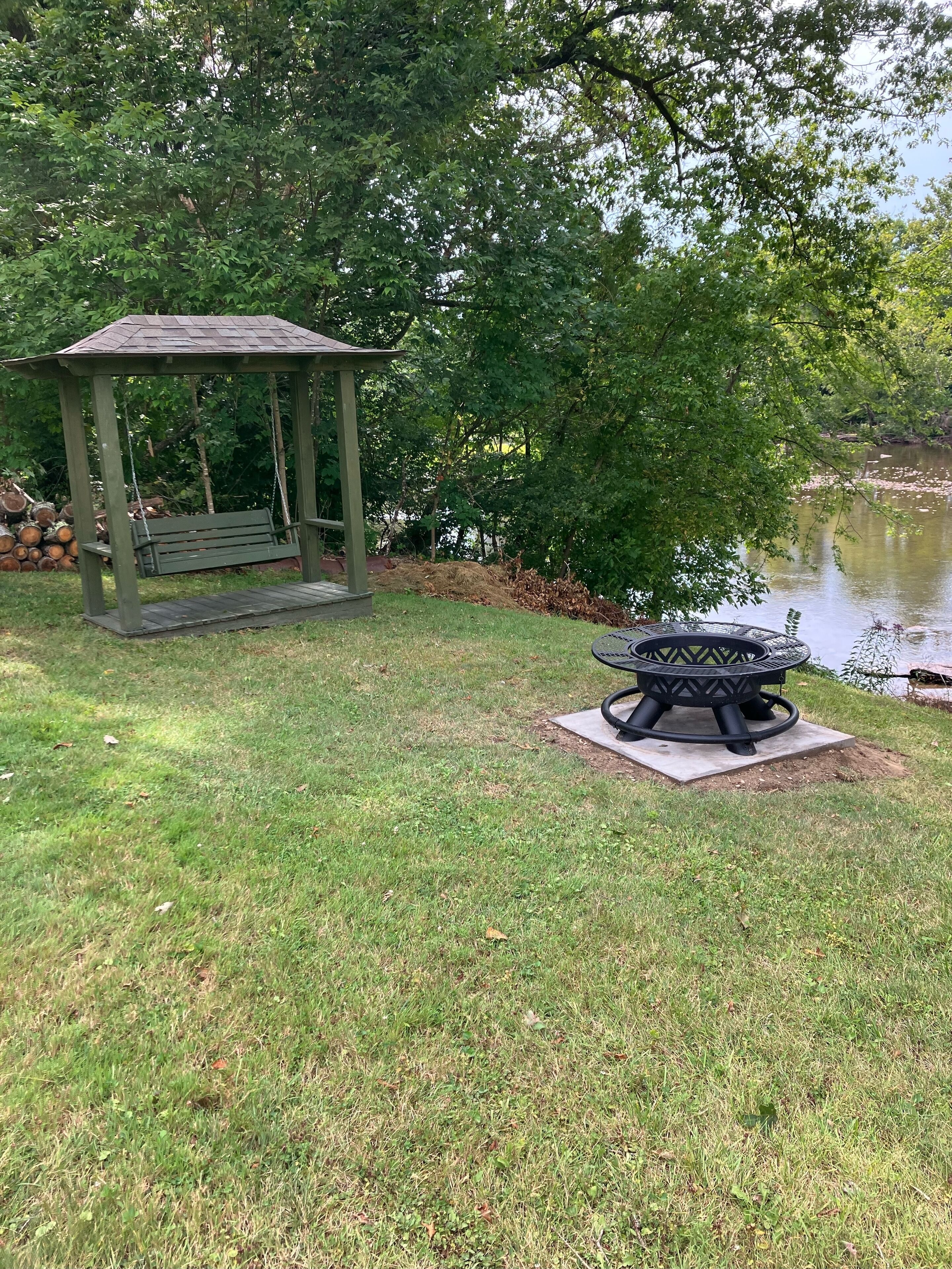 A gazebo, a fire pit, and a pond in a park.