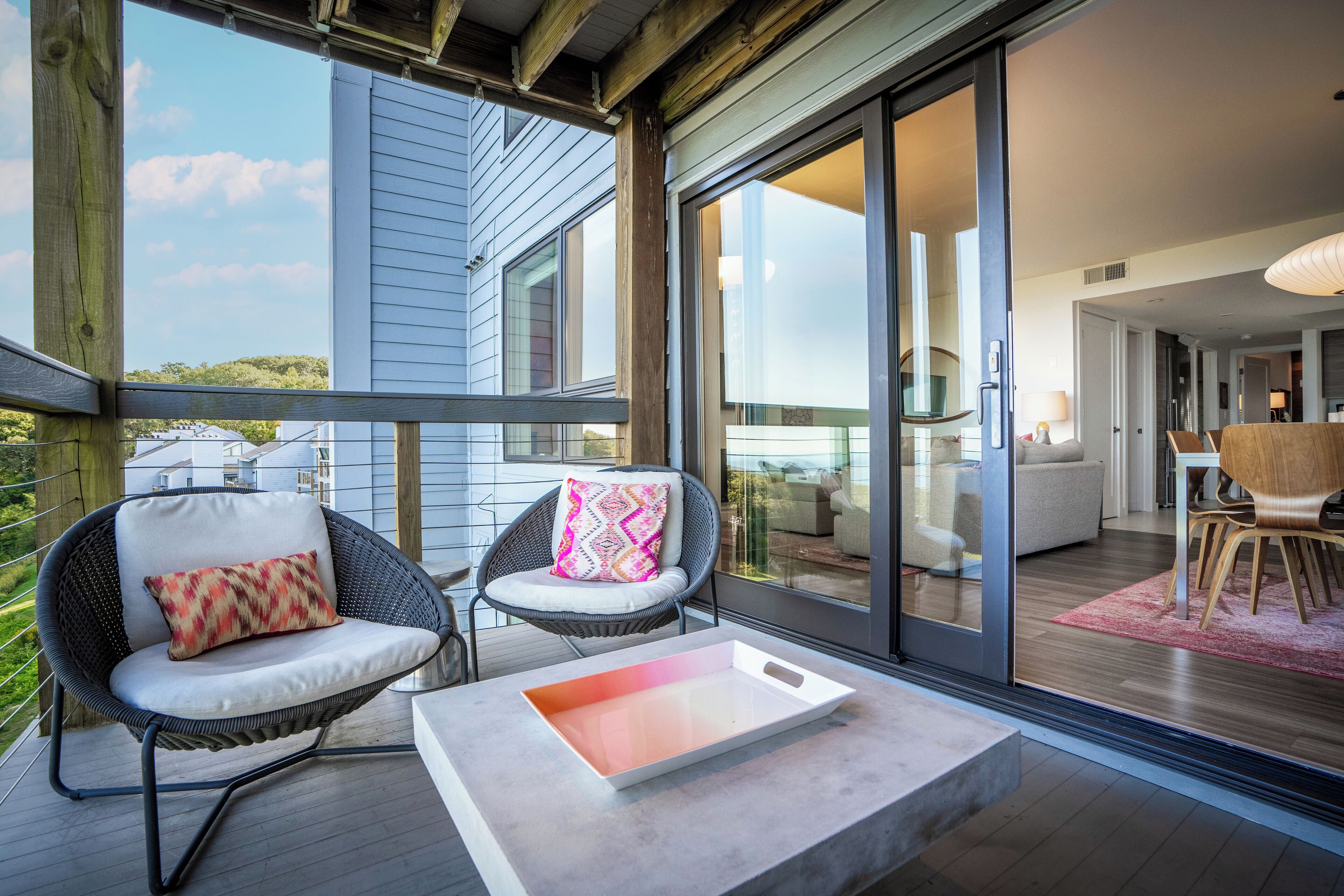 Un espace extérieur moderne, aménagé avec des fauteuils en osier et une table, et de grandes portes-fenêtres coulissantes qui donnent accès à un espace intérieur comprenant un coin repas.