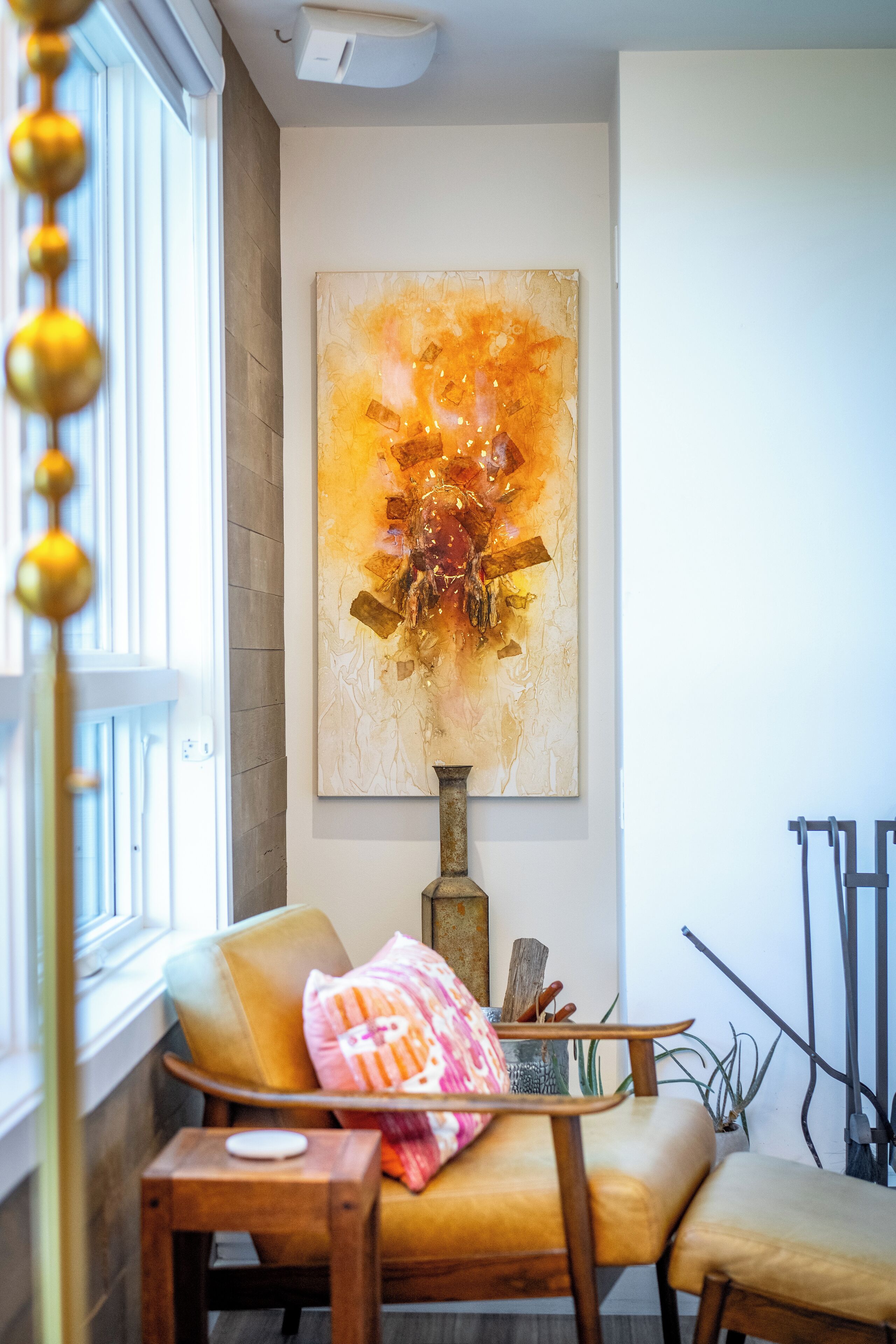 Una habitación con un cuadro abstracto grande, una silla de madera, una mesita y una ventana con vistas.