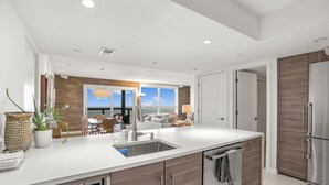 A modern kitchen with a built-in dishwasher, a large island with a sink, wooden cabinets, and a view to the living area. - Luxury Condo in the Sky! Finest in Wintergreen! (Wintergreen Resort)