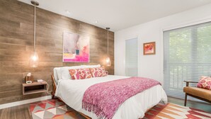 A modern bedroom with a wooden accent wall, a large bed with patterned pillows, a pink throw blanket, and a geometric rug. - Luxury Condo in the Sky! Finest in Wintergreen! (Wintergreen Resort)