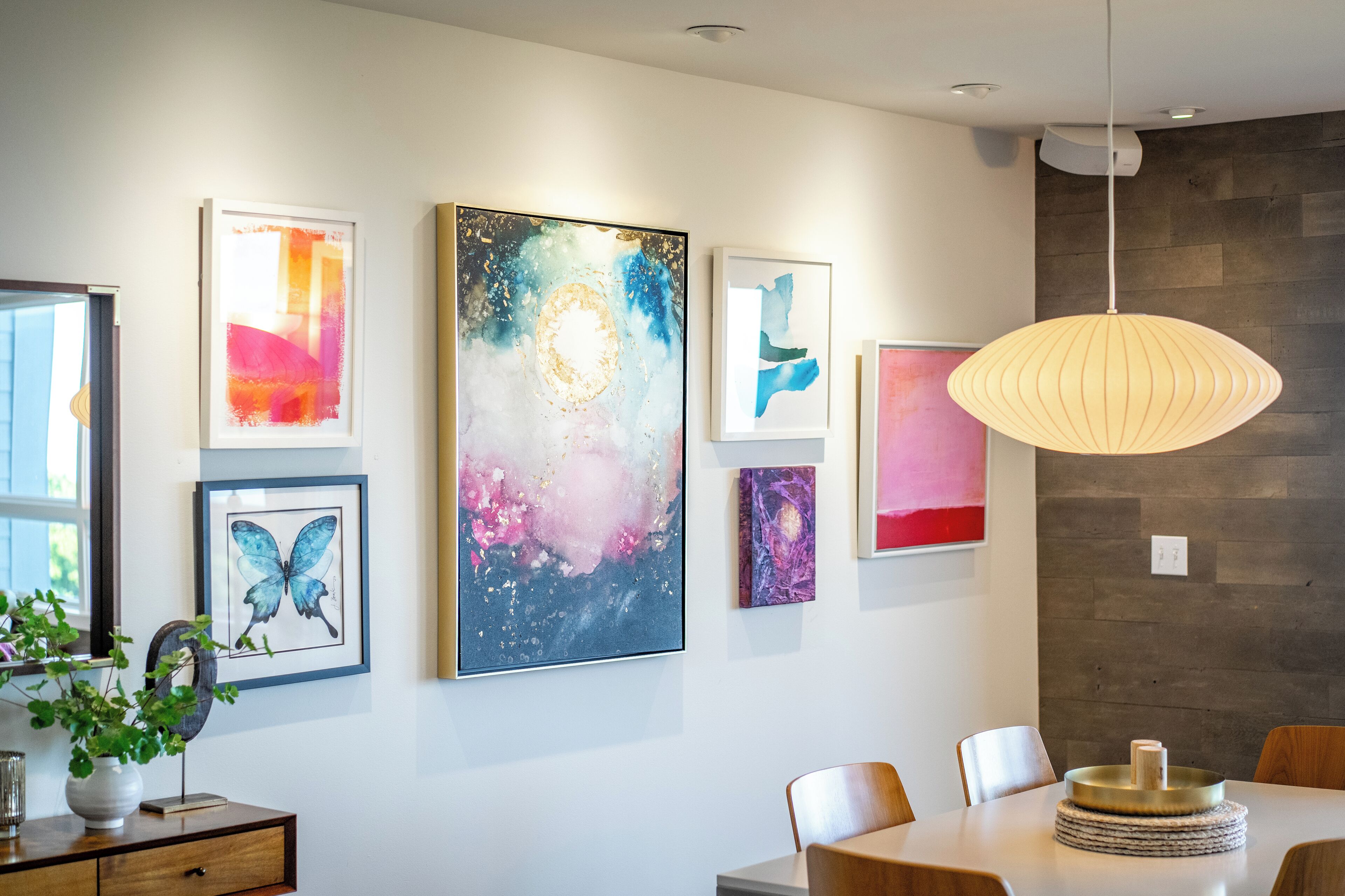 A modern dining area with a white table, wooden chairs, and a hanging pendant light.