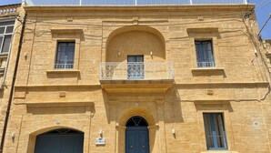A two-story building with a central arched entrance, a blue door, and a balcony with decorative railings. - House of character with pool & jacuzzi for 5 persons, central yet quiet location (Nadur)