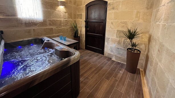 A spa area with a hot tub, stone walls, and a wooden door. - House of character with pool & jacuzzi for 5 persons, central yet quiet location (Nadur)