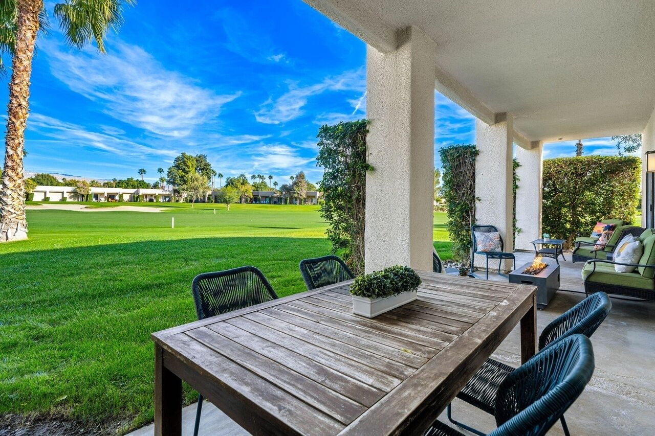 Un patio couvert avec une table et des chaises en bois, un foyer extérieur et une vue sur un terrain de golf.