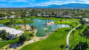 Luftaufnahme eines Golfplatzes mit Teich, Palmen und einem Bergpanorama im Hintergrund.