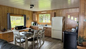 A compact kitchen with wooden cabinets, a refrigerator, a microwave, and a dining area with a table and chairs.