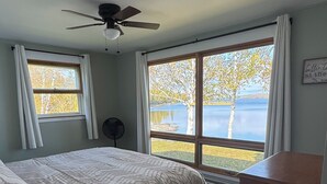 A bedroom with a bed, a ceiling fan, a dresser, and a view of a lake.
