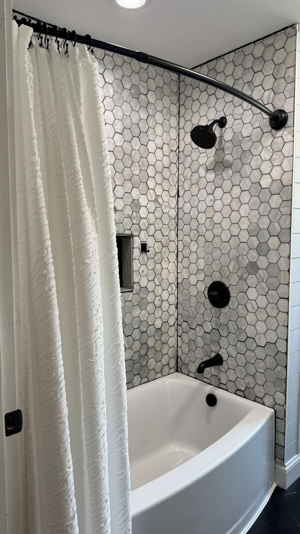 A bathroom with a hexagonal tile wall, a white bathtub, and a shower curtain. - Relax in Aroostook County at this little piece of heaven right on the lake! (Portage Lake)