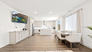 Une cuisine moderne avec des meubles blancs, un îlot central et un coin repas avec des chaises blanches.