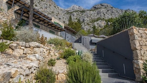 A stone staircase leading up to a building with a metal railing, surrounded by rocky terrain and vegetation.