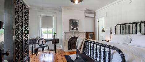 A bedroom with a bed, a fireplace, a desk with a chair, and a window.