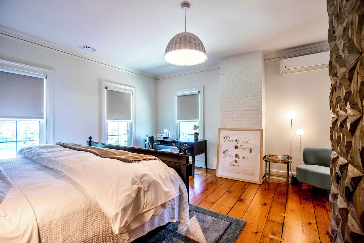 Ein Schlafzimmer mit Bett, Schreibtisch und Stuhl, einem großen Fenster und einer Wand-Klimaanlage.