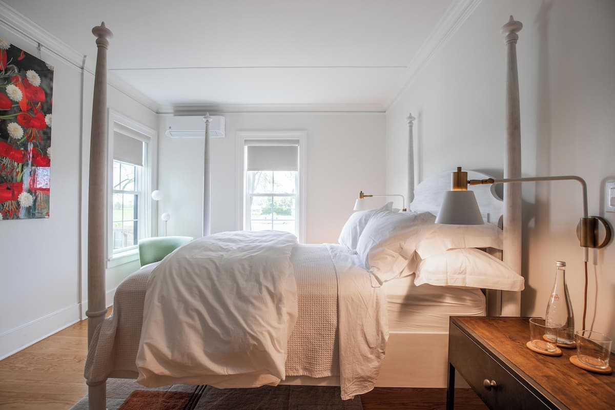 Ein ordentlich eingerichtetes Schlafzimmer mit Bett, Nachttisch, Lampe und einem Fenster mit Blick.