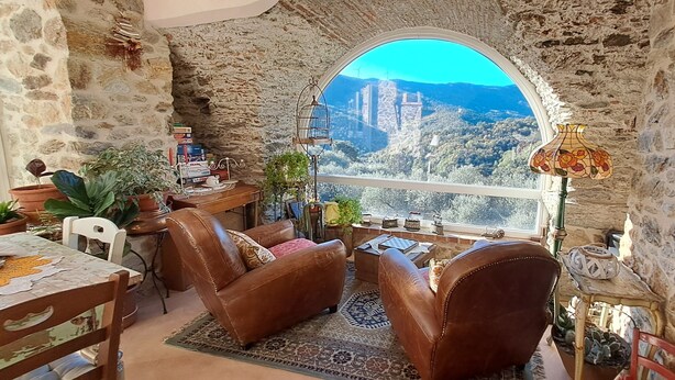 A cozy room with stone walls, a large arched window, leather chairs, a small table, and various decorative items.