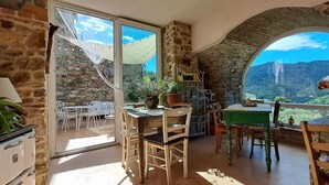 A rustic dining area with stone walls, a table, chairs, and a view of a mountain.