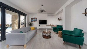 Een moderne woonkamer met een grijze bank, groene fauteuils, een salontafel en een televisie aan de muur.
