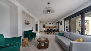 Een moderne woonkamer met een grijze bank, groene fauteuils en een eetgedeelte met een houten tafel en stoelen.