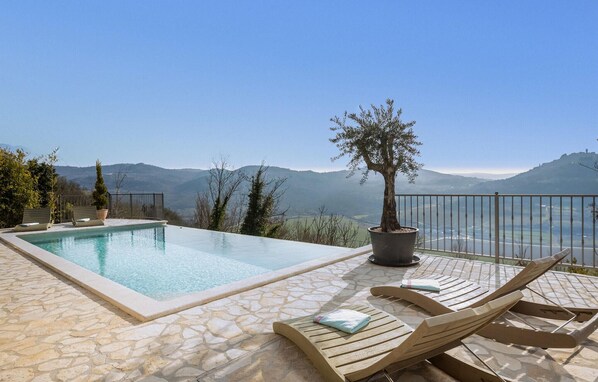 A poolside area with a stone floor, lounge chairs, and a potted tree.