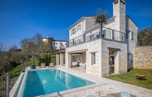 A two-story stone house with a swimming pool, outdoor seating, and a stone fireplace.