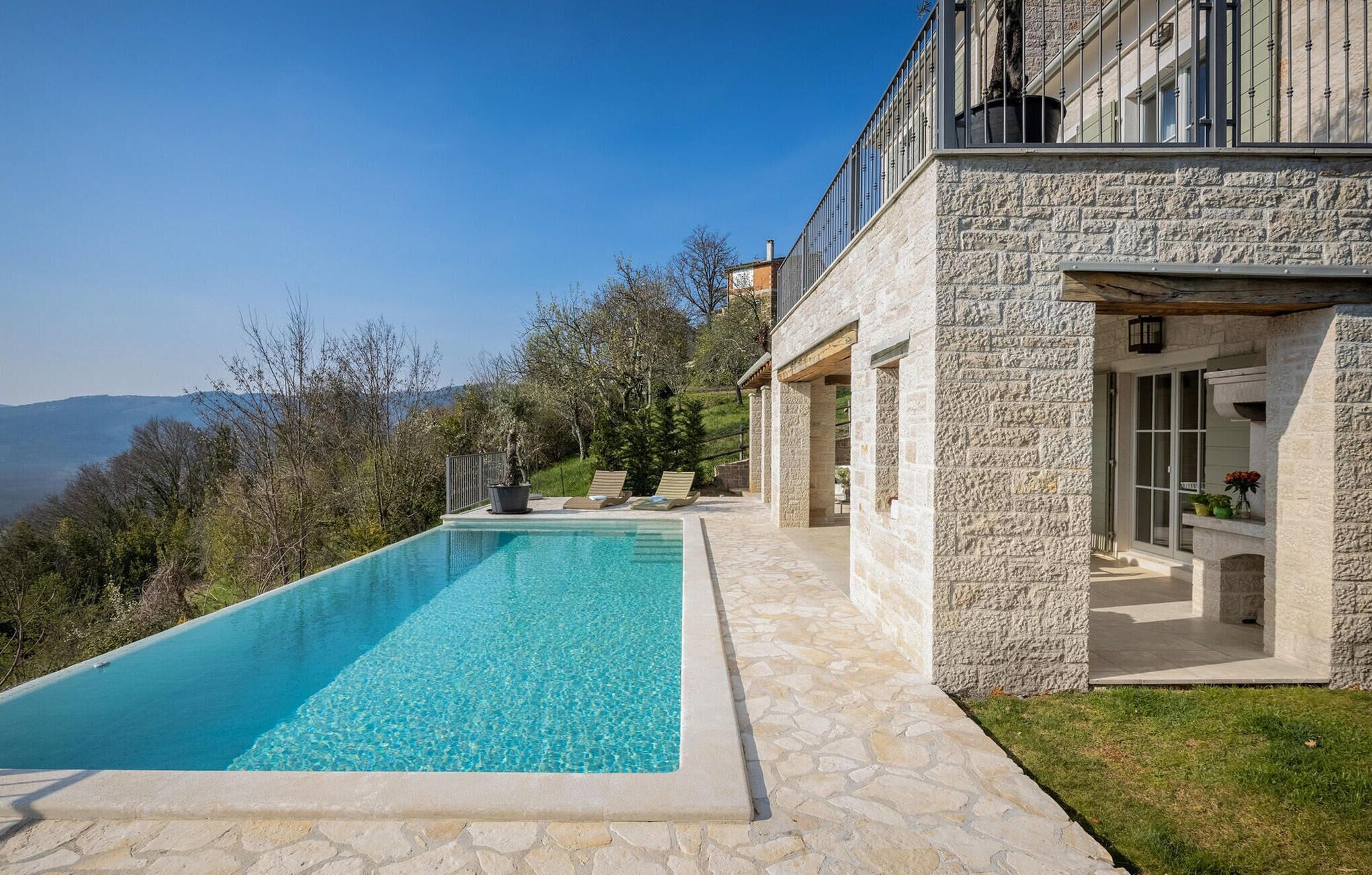 A modern stone building with a swimming pool, outdoor seating, and a view of the mountains.