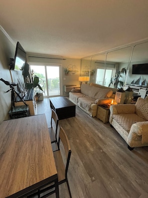 Relax in this stylish living room with a sofa set, dining table, and flat-screen TV, plus a balcony with a view of lush greenery.