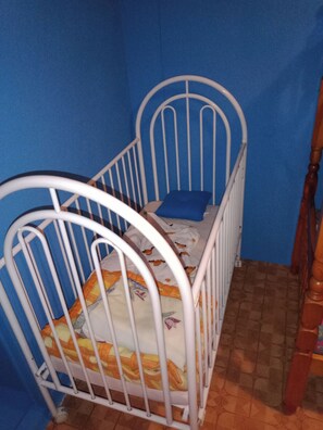A white metal crib with a blue mattress and a blue pillow against a blue wall. - Maison Complète (Montluçon)