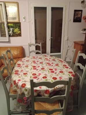 A dining area with a round table covered by a floral tablecloth, surrounded by wooden chairs. - Maison Complète (Montluçon)