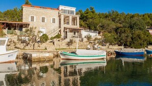 A stone building with a balcony, a staircase leading to the upper floor, and boats docked in the water.