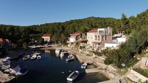 A coastal village with stone buildings, a marina with boats, and a forested hillside.
