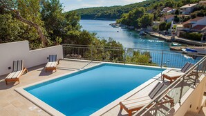 A rectangular swimming pool with a tiled edge, surrounded by lounge chairs and a metal railing.