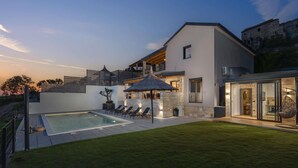 Ett modernt hus med en swimmingpool, utomhusmöbler och en fasad av sten.