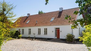 Un bâtiment blanc avec un toit recouvert de tuiles rouges, une porte rouge et une allée pavée.