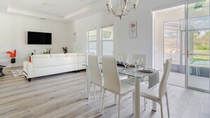 A modern living room with a glass dining table, white sofas, and a flat-screen TV mounted on the wall. - Serenity Lake (Clermont)