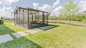 A modern glass-enclosed structure with outdoor seating, a pond, and a grassy area. - Serenity Lake (Clermont)