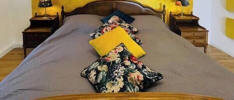 A bed with a wooden headboard, a floral pillow, and a yellow pillow. There are two bedside tables with lamps.