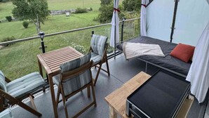 En balkon med et bord, stole, en sofa og udsigt over et grønt landskab.