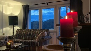 En hyggelig stue med sofa, sofabord, lampe og et vindue med udsigt til naturen.