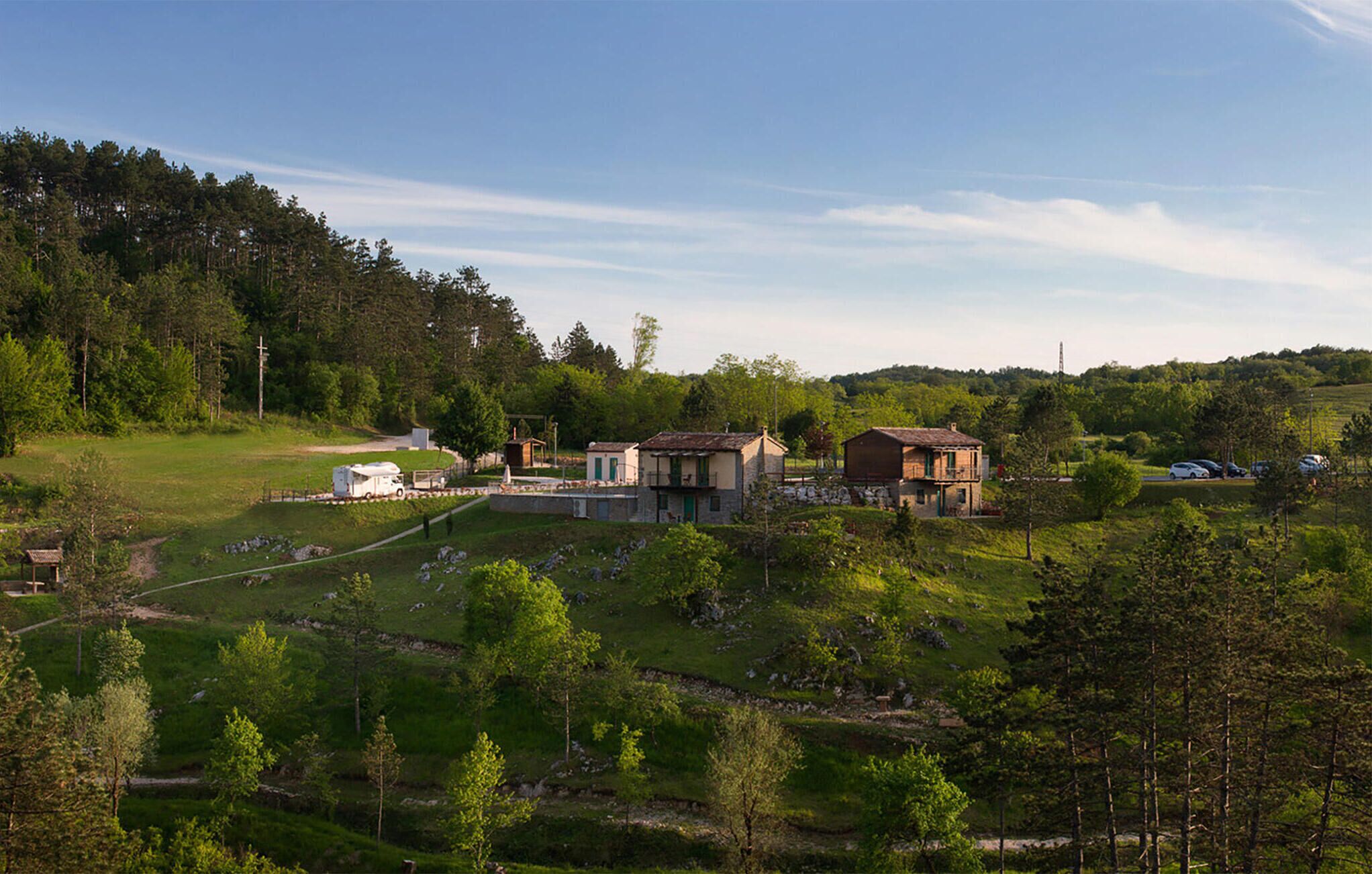 A rural setting with a small cluster of buildings, including a house with a balcony and a barn-like structure.
