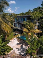 A modern building with a pool, surrounded by lush greenery and palm trees.